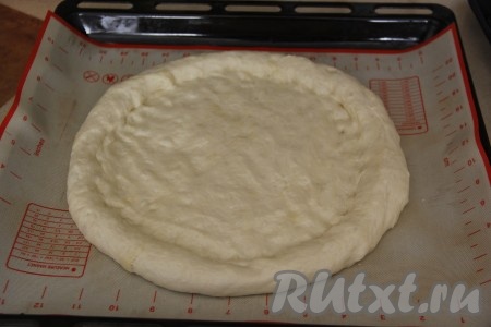 Противень застелить пергаментом (или ковриком для выпекания). Выложить тесто на противень и руками, смазанными растительным маслом, сформировать круглую пиццу диаметром 28 см с пышным краем. Оставить основу на 20 минут в тёплом месте.