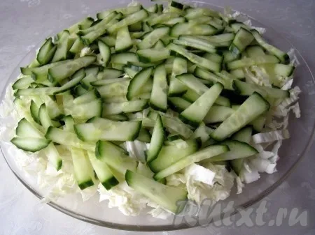 Нашинковать пекинскую капусту и выложить на плоскую тарелку первым слоем. Следующий слой - огурцы, нарезанные соломкой. 