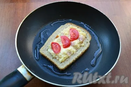 На разогретую с растительным маслом сковороду выложить ломоть хлеба без мякоти. Отверстие в хлебе наполнить сырно-колбасной массой, сверху разместить по 2-3 полукружочка свежего помидора. 