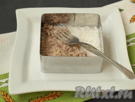 Варёный рис выложить на тарелку с помощью формочки. Разровнять поверхность. С сайры слить масло и размять рыбу вилкой. Выложить сайру поверх риса и также разровнять вилкой. 