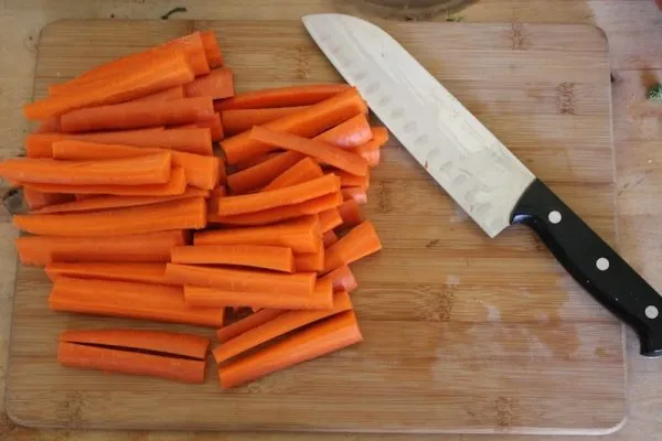 Нарезанная длинными полосками сырая морковь и нож на разделочной доске