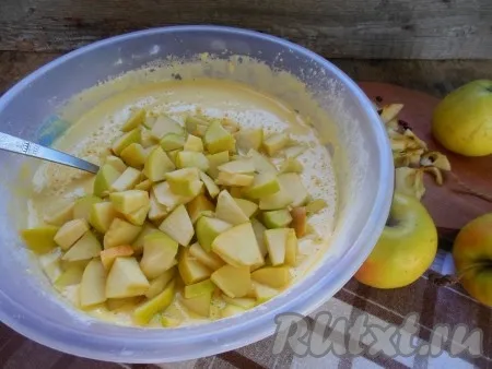 Добавьте яблоки в тесто и перемешайте ложкой, чтобы кусочки яблок равномерно распределились. 