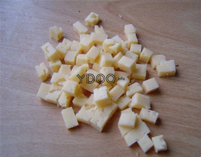 твердый сыр, нарезанный кубиками, лежит на деревянной доске