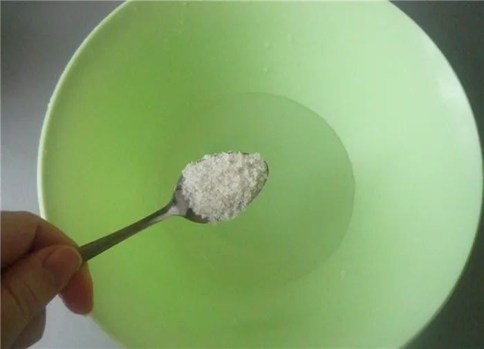 ложка соли всыпается в зеленую пластиковую миску с водой