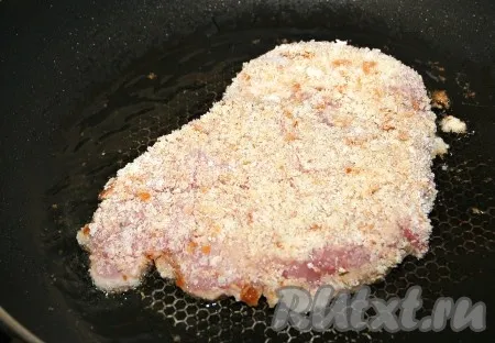 Разогреть масло на сковороде и в раскалённое масло выложить запанированные стейки из свинины. 