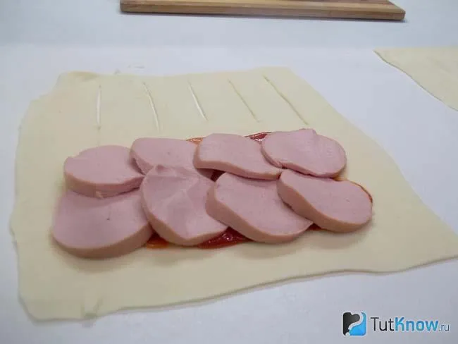Тесто раскатано и на него выложена нарезанная колбаса
