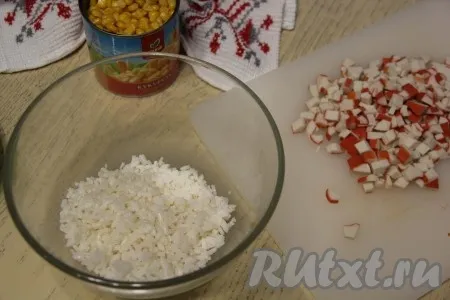 Пока ракушки остывают, можно заняться начинкой закуски. Остывший рис выложить в достаточно глубокую миску. Крабовые палочки мелко нарезать и выложить к рису.