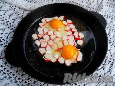 Затем на сковороду с обжаренными крабовыми палочками аккуратно разбейте яйца, стараясь, чтобы желтки остались целыми. 