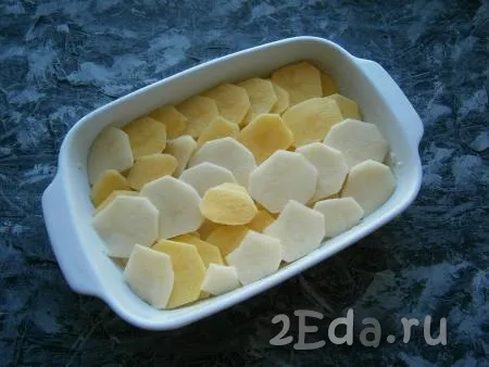 Очистить картошку и нарезать тонкими кружочками. Кружочки картофеля выложить в форму внахлест. Обычно картошка выкладывается в форму в один слой, но, если форма небольшая, можно выложить и в 2 слоя (если выкладываете картошку в два слоя, тогда первый слой посолите).