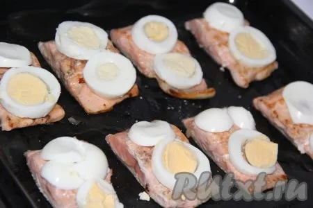 Обжаренные кусочки рыбы выложить на противень, смазанный маслом. Варёные яйца очистить и нарезать тонкими кружочками. Выложить на каждый кусочек рыбы по 2 кружочка яйца. 