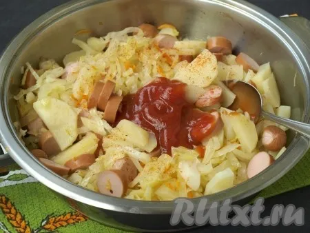 Посыпать блюдо молотым перцем, добавить томатный кетчуп, перемешать, снова накрыть сковороду крышкой и тушить капусту с картошкой и сосисками 8-10 минут. 