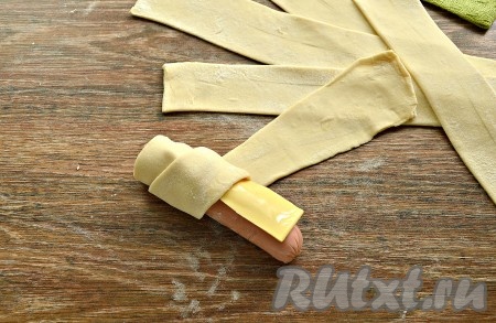 На сосиску поместить кусочек сыра и обернуть сосиску с сыром по спирали полоской слоёного теста. 