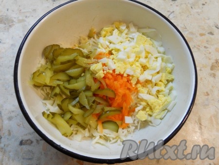 Очищенные рубленые вареные яйца и нарезанные небольшими кусочками соленые огурцы выложить в салат из свежей капусты и моркови. 