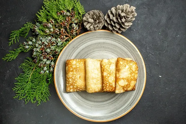 horizontal view of delicious meat filled pancakes on a white plate and conifer cone on black background - Блинчики с рыбой и рисом