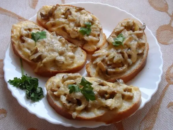 Готовые горячие бутерброды с шампиньонами, сыром и зеленью на белой тарелке