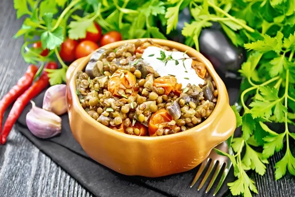 green lentils stewed with eggplant tomatoes garlic and spices sour cream sauce in bowl on board - Тушёная чечевица с овощами в мультиварке