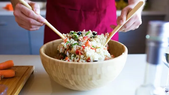 Молодой человек готовит салат с овощами и киноа