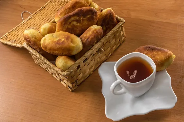 traditional homemade baked patties or pies with jam in a wicker basket next to a white cup of tea - Монастырские жареные пирожки с повидлом